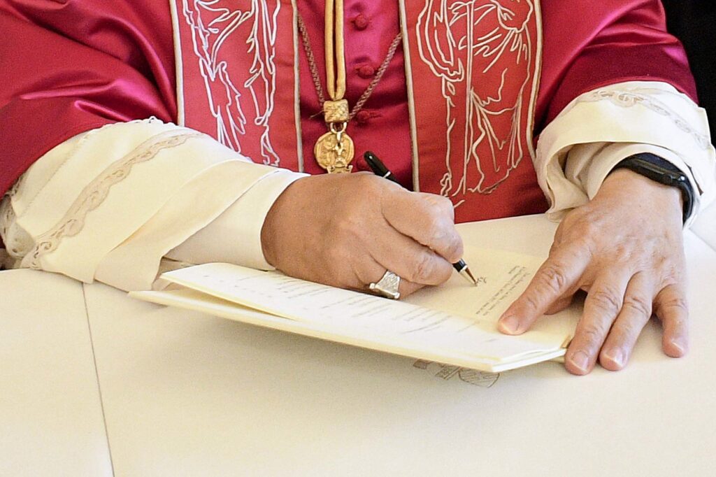 Pope Leo XIV signs his first apostolic exhortation, "Dilexi Te" ("I Have Loved You"), in the library of the Apostolic Palace at the Vatican October 4, 2025, the feast of St. Francis of Assisi, as Archbishop Edgar Peña Parra, the substitute secretary for general affairs at the Vatican Secretariat of State, looks on. The exhortation was be released October 9. Photo: OSV News photo/Vatican Media/CPP