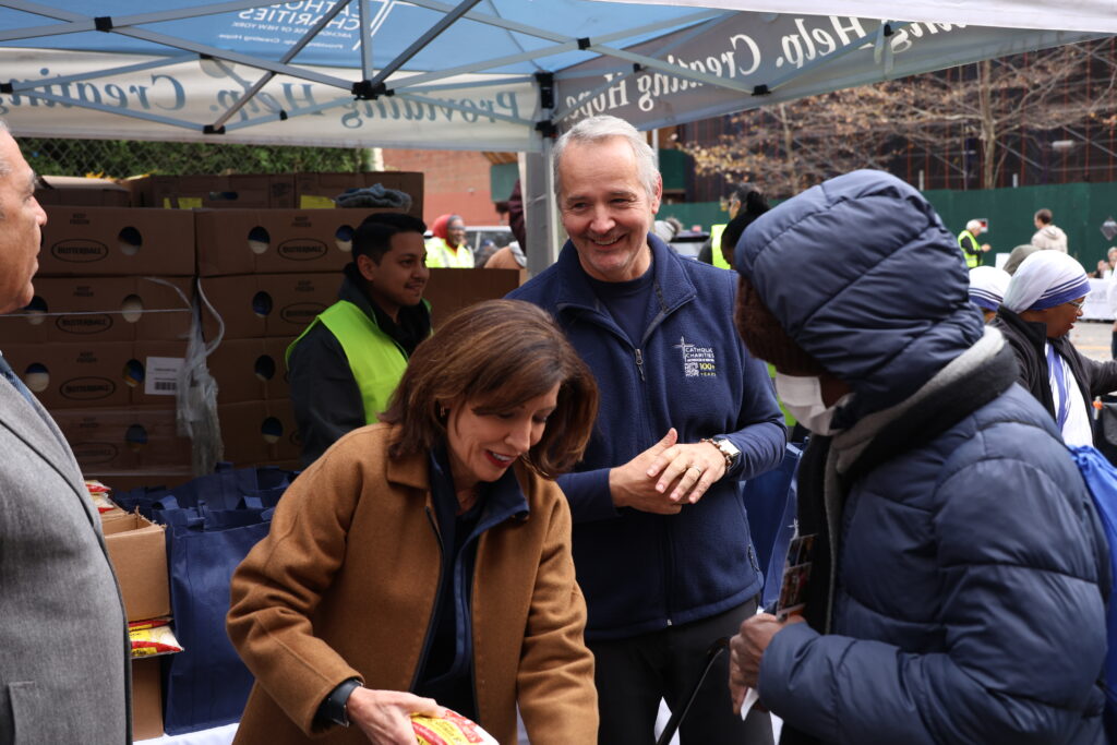 New York Governor Kathy Hochul (center) and Catholic Charities of New York CEO J. Antonio Fernandez load food for a participant in a pre-Thanksgiving distribution in central Harlem on November 25, 2025.
