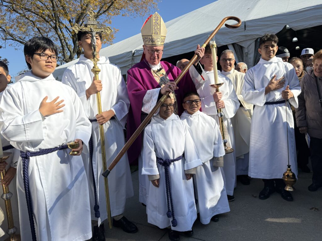Cardinal Timothy Dolan (center) poses with altar servers from St. Raymond's Church in the Bronx, after an All Souls' Day Mass at St. Raymond's Cemetery, November 2, 2025.