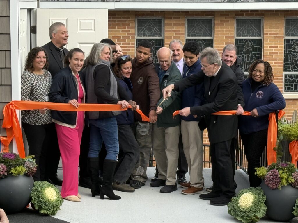 Father Bob Norris (center right, holding scissors) cuts the ribbon, opening Our Lady of Mount Carmel-Elmsford Food Pantry’s new storage space, as Auxiliary Bishop John Bonnici (left, back row) and pantry organizers and volunteers look on, November 5, 2025.