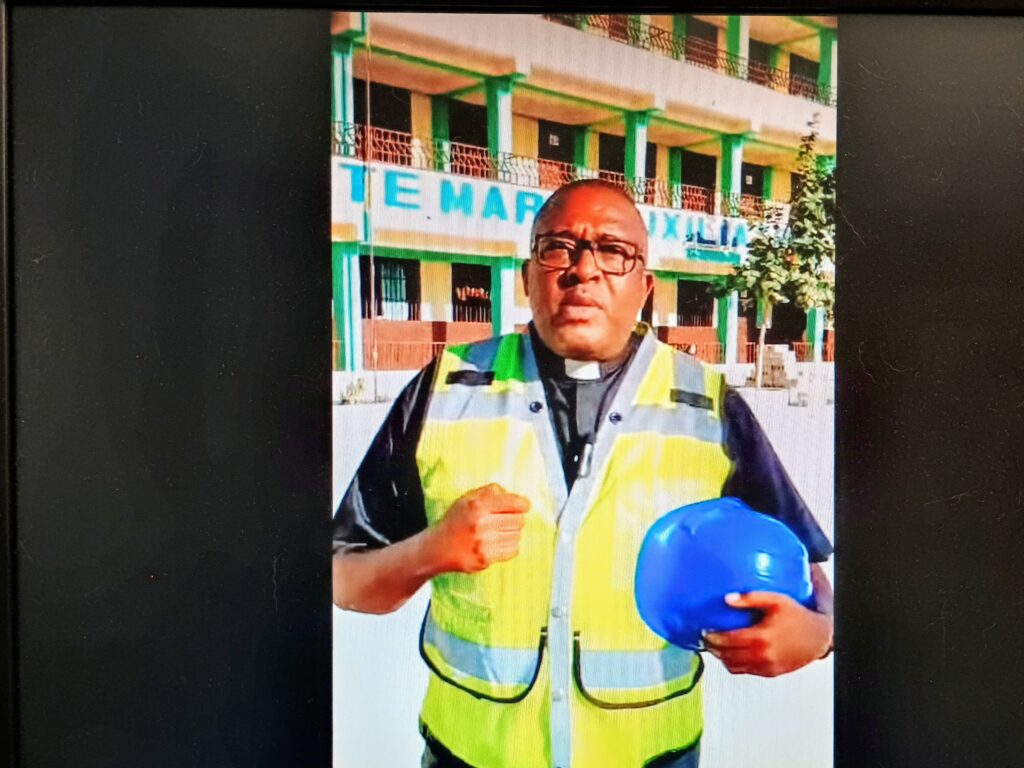 A screenshot shows Father Edouard Ducarmel of Our Lady Help of Christians parish in Cité Soleil Haiti, giving a video tour of construction work completed with the assistance of the Church of St. Clare in the Great Kills area of Staten Island.