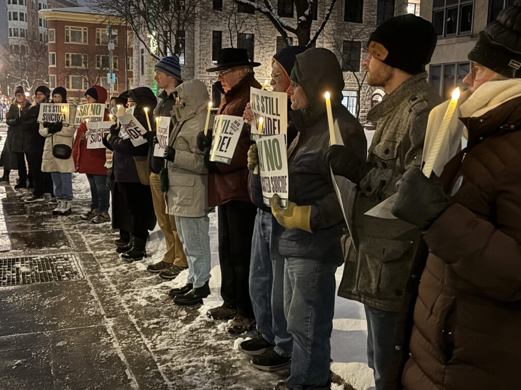 People attend a candlelight vigil outside the Senator John H. Hughes Office Building in downtown Syracuse on December 4, 2025, to speak out against a controversial bill that, should it become law, would allow physicians to assist terminally ill adults as young as age 18 to die by suicide.