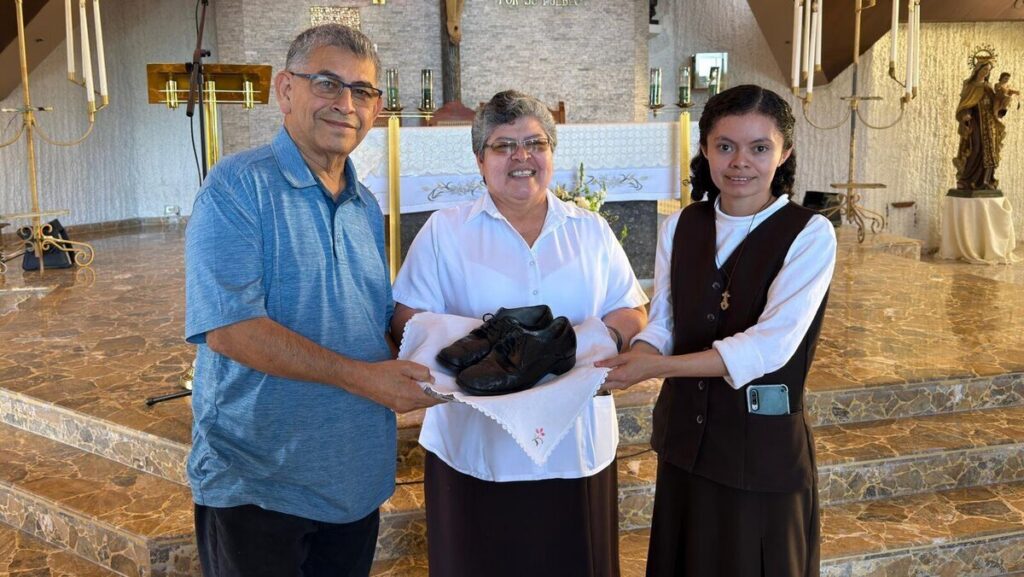 El hermano franciscano Octavio Durán entrega los zapatos que llevaba San Óscar Romero cuando fue martirizado a la hermana Tránsito de la Cruz (centro), superiora de la comunidad local de las Carmelitas Misioneras de Santa Teresa, y a la hermana Reina Mancía, encargada del museo conmemorativo del Hospital Divina Providencia de San Salvador, El Salvador. (Foto OSV News / cortesía de Octavio Durán, Revista Misioneros/Maryknoll Magazine)