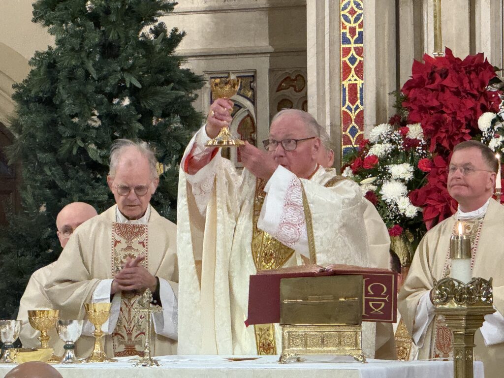 Cardinal Timothy Dolan (center) raises the chalice during the Liturgy of the Eucharist, flanked by Auxiliary Bishop Peter Byrne (left) and Auxiliary Bishop Edmund J. Whalen, vicar for clergy (right), on December 20, 2025, at the Church of St. Augustine in Larchmont.