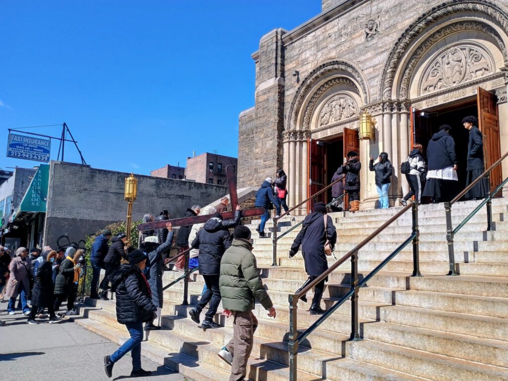 La procesión del Vía Crucis de Washington Heights/Inwood llegando a la Iglesia del Buen Pastor la mañana del sábado 28 de marzo de 2026. Algunos participantes se turnaron para llevar la cruz. Foto por Armando Machado/The Good Newsroom
