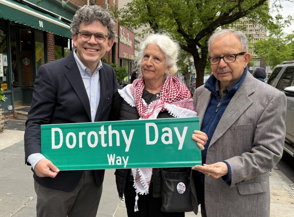 Martha Hennessy, granddaughter of Dorothy Day, holds a replica of the "Dorothy Day Way" street sign May 2, 2026, with Councilman Lincoln Restler, left, and Alex Avitabile, a board member of the Dorothy Day Guild, in the Brooklyn Heights section of New York City. Hennessy says it's "very surreal" to be part of a family of someone being considered for sainthood.