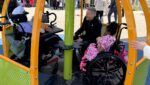 Archbishop Ronald Hicks (in black) rides a merry-go-round at Elizabeth Seton Children’s with the center’s international ambassador Stephanie and a resident, May 4, 2026.