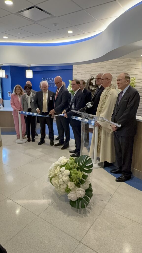 ArchCare CEO Scott LaRue (center left, with scissors), Calvary Hospital President Michael J. Fosina, MPH, FACHE (center), and Calvary Hospital Chairman Jeffrey Menkes (center right) cut the ribbon marking the official opening of Calvary Hospital’s new lobby and family lounge on Wednesday, May 13, 2026.