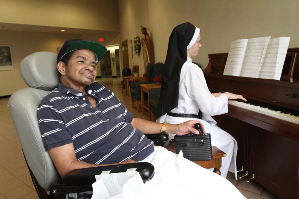 In this file photo, patient Warren Saunders smiles as Dominican Sister Agnes Mary plays the piano at Rosary Hill Home in Hawthorne, where the nursing home staff provides palliative care to people with incurable cancer. Four orders of women religious and Catholic healthcare ministries filed suit in federal court in Albany July 17, 2026, arguing that New York’s new assisted dying law would force them to choose between their faith and their ability to provide care for the sick, the elderly, and the dying.