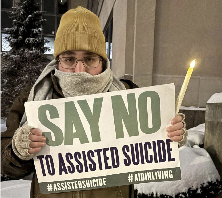 A demonstrator against assisted suicide displays a sign during a candlelight vigil outside the Sen. John H. Hughes Office Building in downtown Syracuse on Dec. 4, 2025. New York's new medical assistance in dying law goes into effect on Aug. 5, 2026.