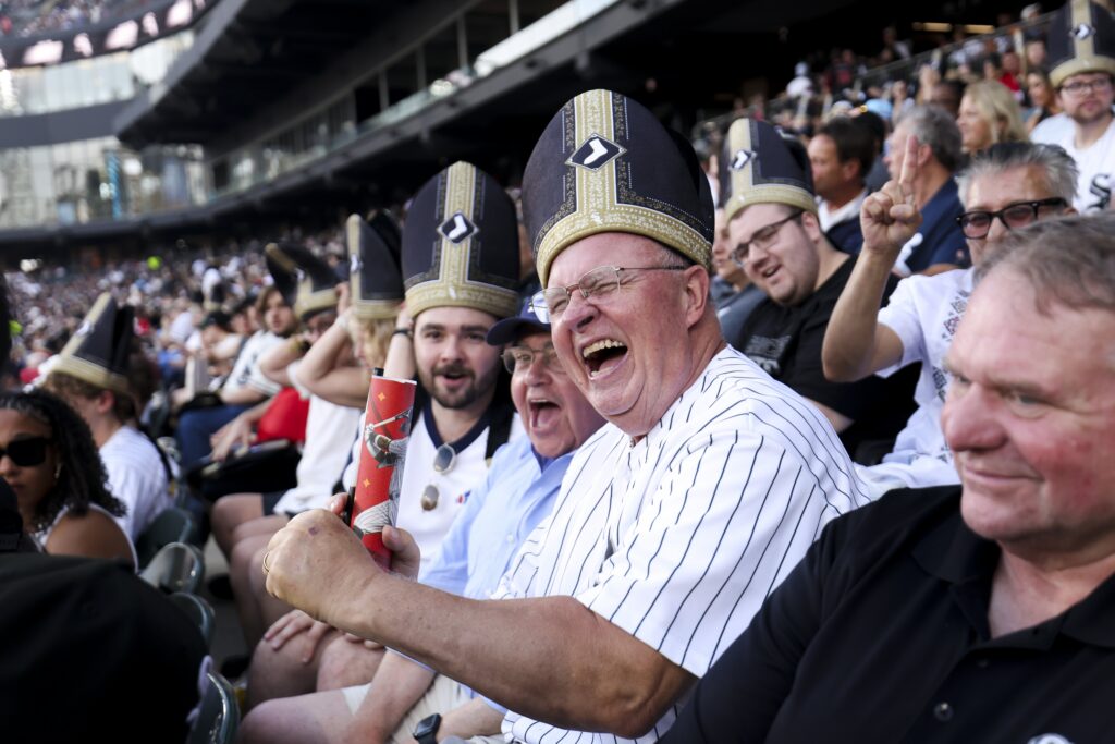 White Sox fans smile while wearing "pope hats" at an Aug. 11, 2026, baseball game at Rate Field in Chicago. The White Sox game paid tribute to Pope Leo XIV, a native of Dolton, Ill., with a first pitch thrown by a nun, a performance by the ChiTown Popes, and a fifth inning "sign of peace" while taking on the Cincinnati Reds.