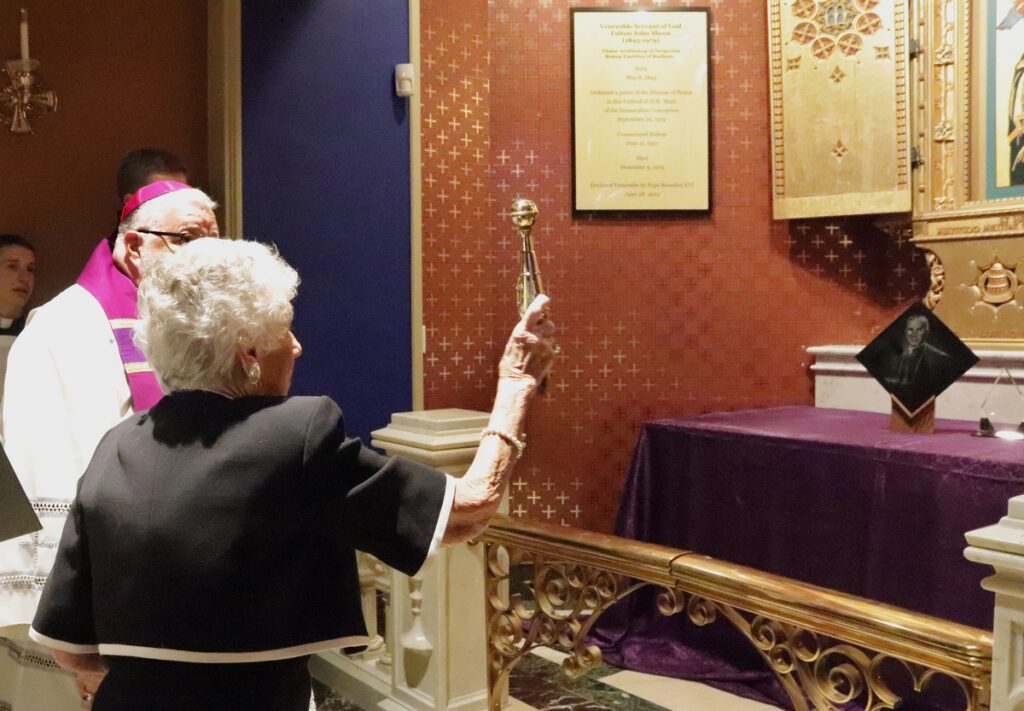 El obispo Daniel R. Jenky, de Peoria (Illinois), observa cómo Joan Sheen Cunningham, sobrina del difunto arzobispo Fulton J. Sheen, rocía con agua bendita la nueva tumba que alberga los restos de su tío en la catedral de Santa María de Peoria, el 27 de junio de 2019. (Foto CNS/Jennifer Willems, The Catholic Post)