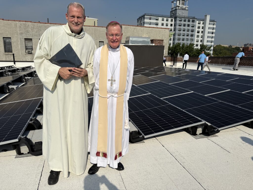 Bishop Edmund Whalen (center), vicar general of the Archdiocese of New York, and Fr. Willem Klaver, pastor of the parish of St. Charles Borromeo, Resurrection, and All Saints in Harlem, stand with the Church of the Resurrection’s new solar panel installation on Thursday, September 18, 2026.
