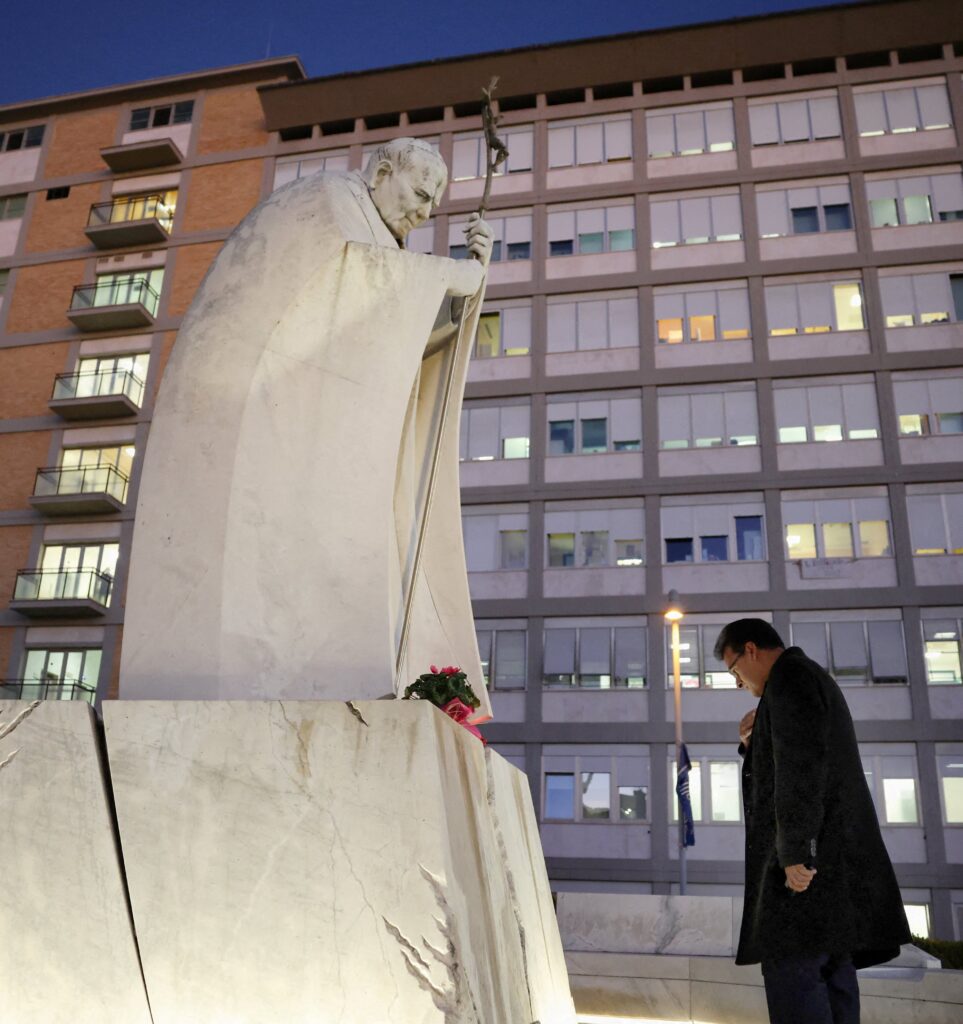 Un hombre reza ante una estatua de San Juan Pablo II frente al Hospital Gemelli de Roma el 13 de octubre de 2026, donde el Papa León XIV fue operado esa misma tarde para extirparle un nódulo pulmonar. Esa misma noche, el Vaticano confirmó que el Papa León padece cáncer de pulmón.